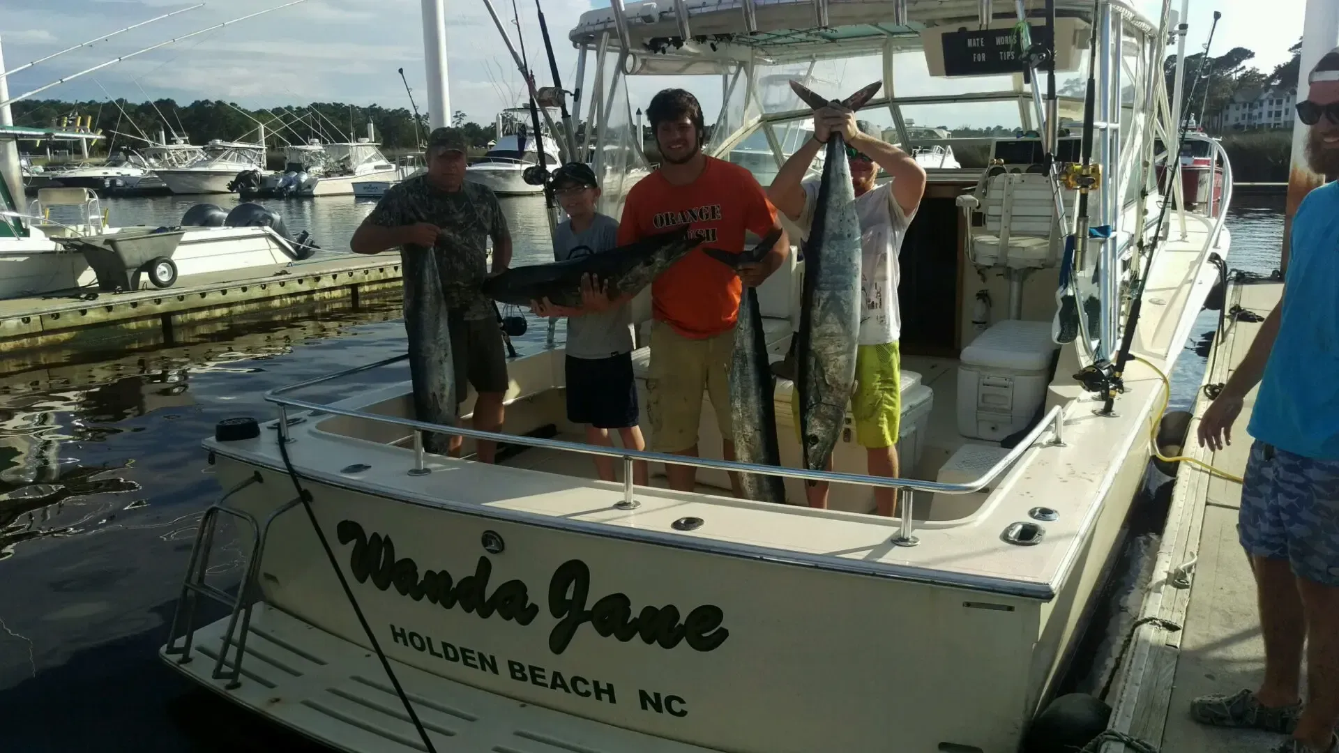 People on a white fishing boat docked at a marina, with boats and water in the background.