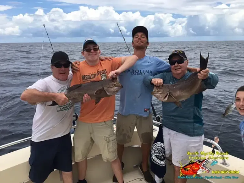 Four people on a boat holding large fish, smiling on the ocean under cloudy skies.