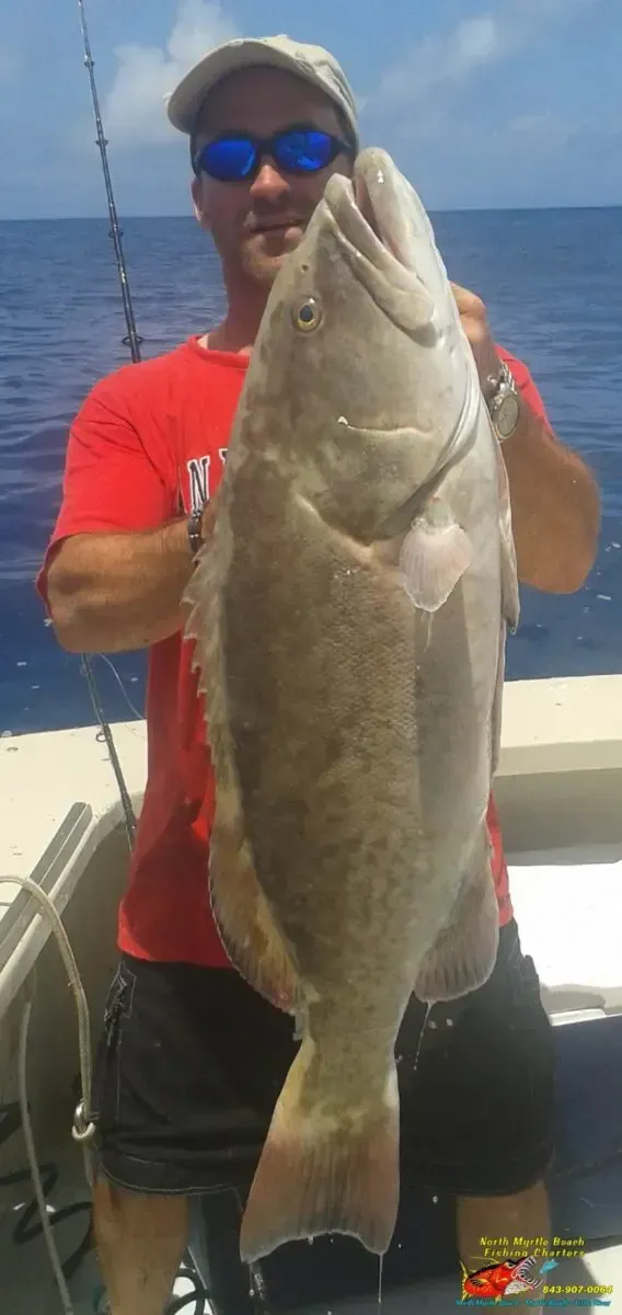 Man holding a large fish on a boat with ocean and blue sky in the background