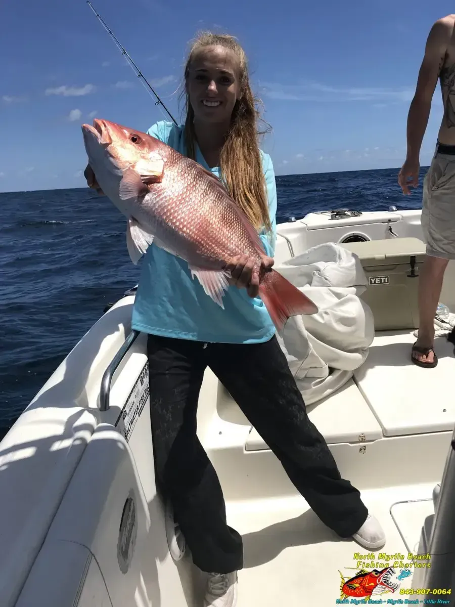 Person on a boat holding a large pink fish on a sunny ocean day