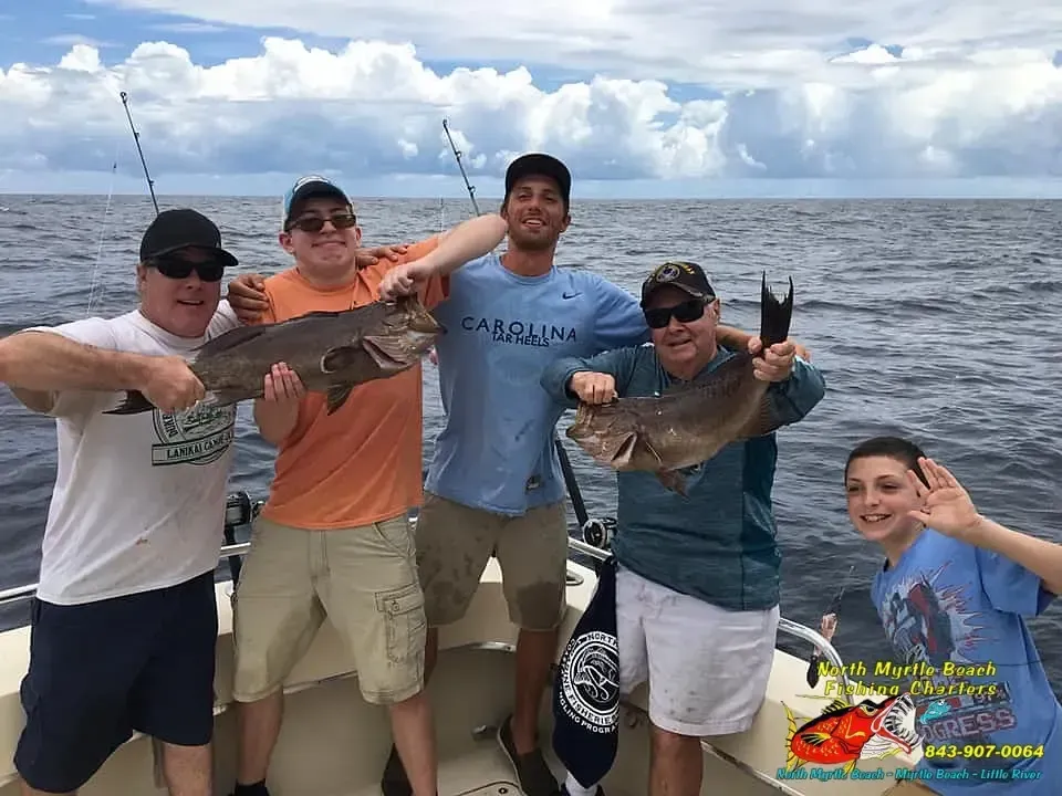 Five people on a boat holding up fish, smiling on a cloudy ocean day