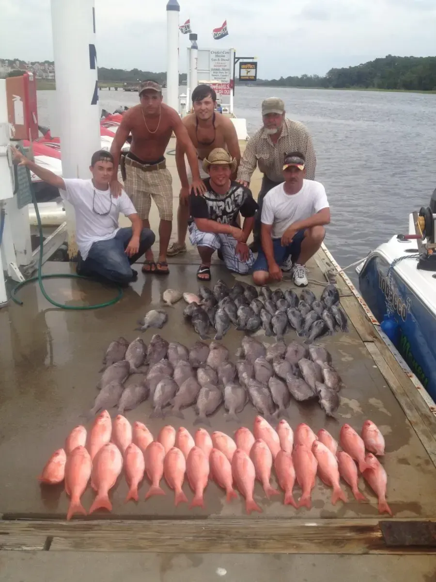 Group posing with a large catch of fish on a riverboat dock.