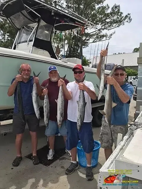 Four people holding large fish beside a boat at a marina