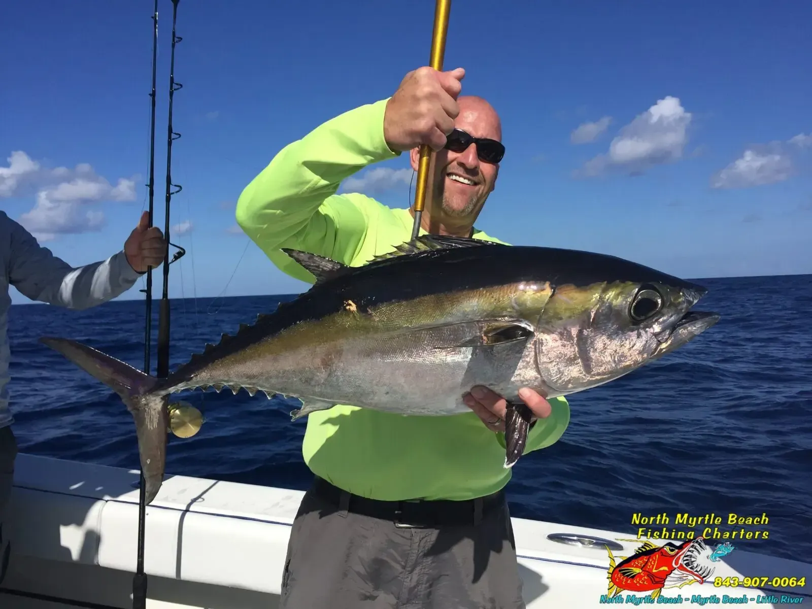 Angler holding a large tuna on a boat at sea under a blue sky