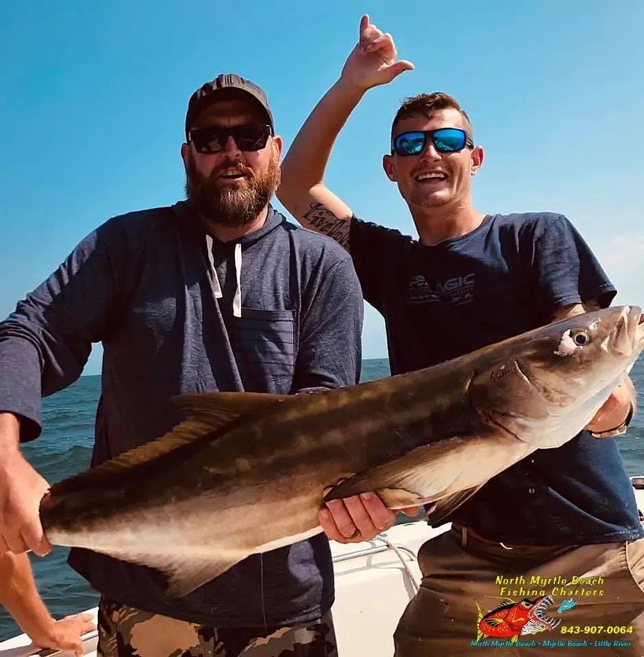 Two people on a boat holding a large fish, smiling on a sunny day