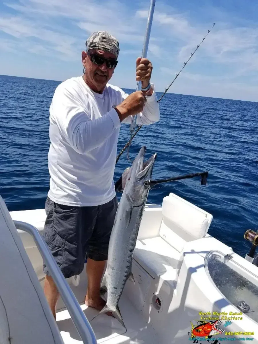Man on a boat holding a large fish over the ocean, with blue water and sky in the background