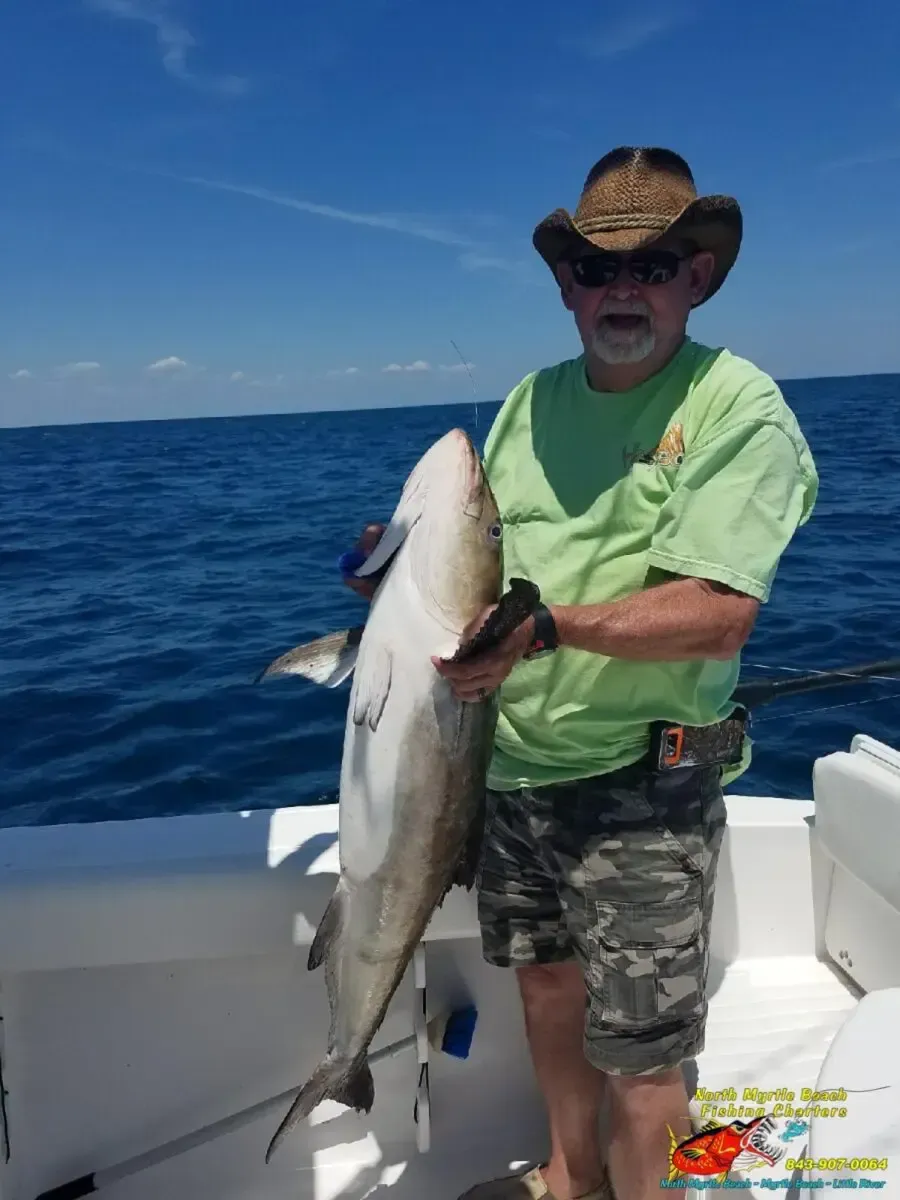 Man on a boat holds a large fish over open blue ocean under a clear sky