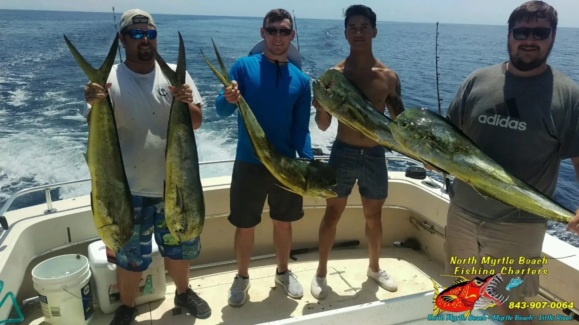 Four anglers on a boat holding large colorful fish on a sunny day at sea