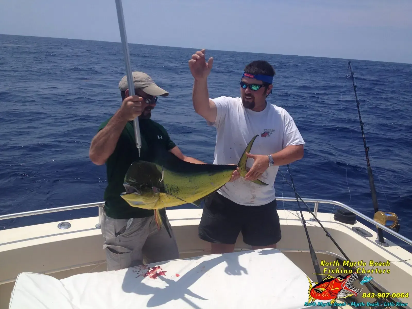 Two anglers on a boat hold up a large yellow fish on the open ocean.