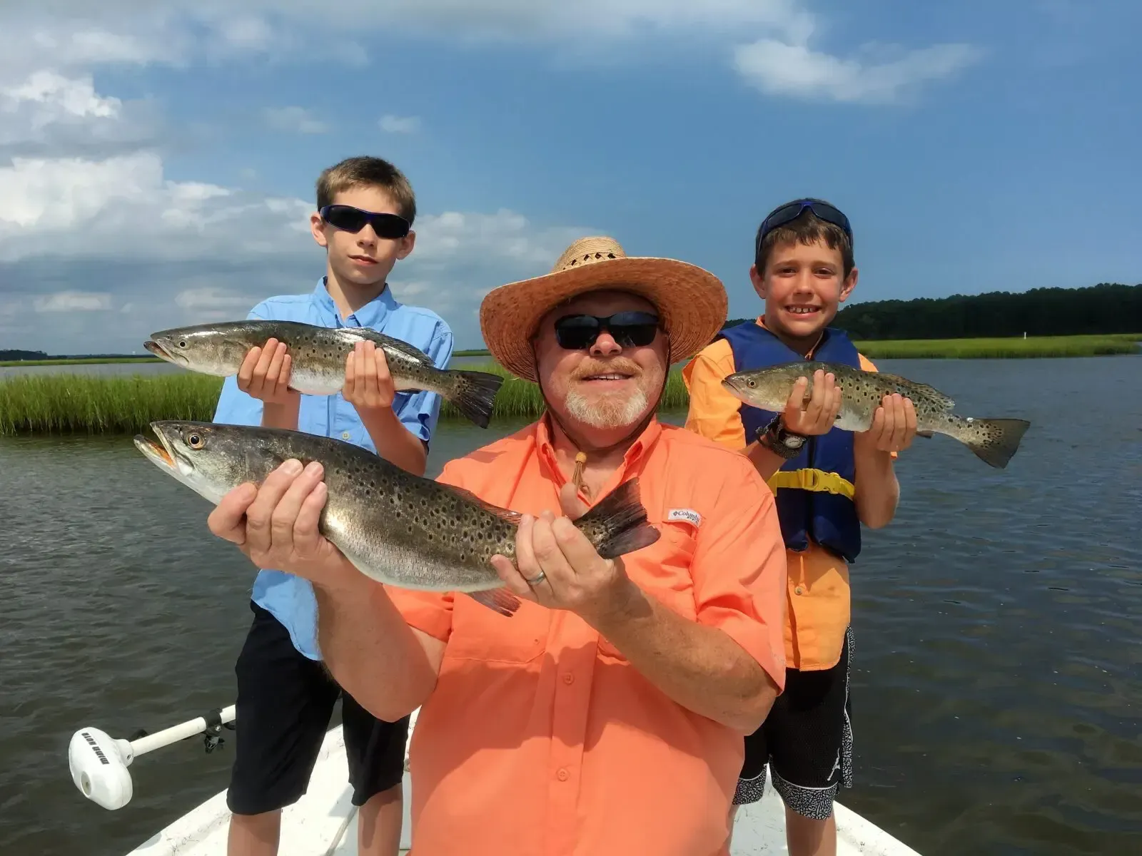 Three people on a boat holding large fish on a sunny lake.