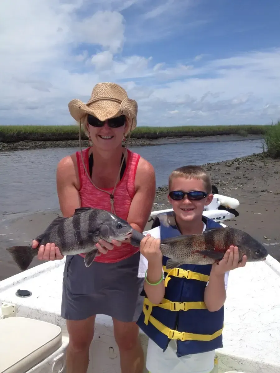 Woman and child on a boat holding fish, wearing hats and sunglasses on a sunny river.
