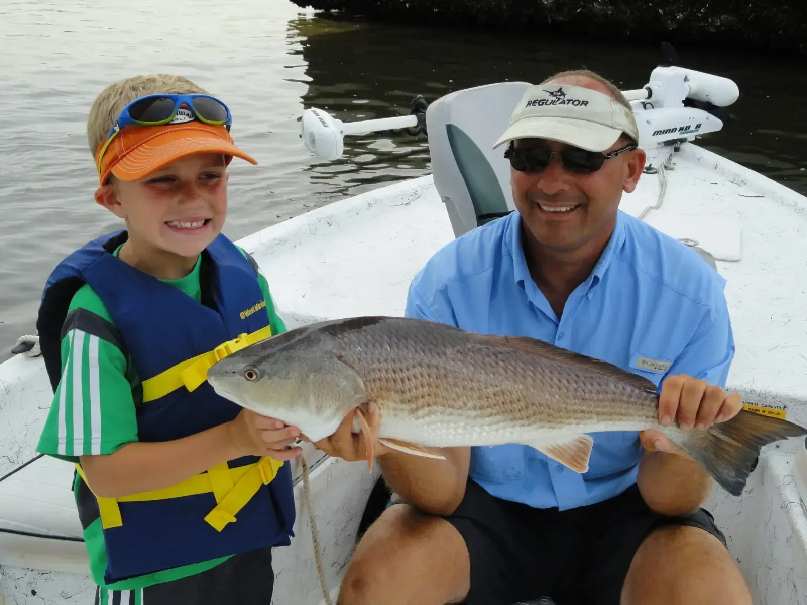 Two people on a boat holding a large fish, with water and another boat in the background