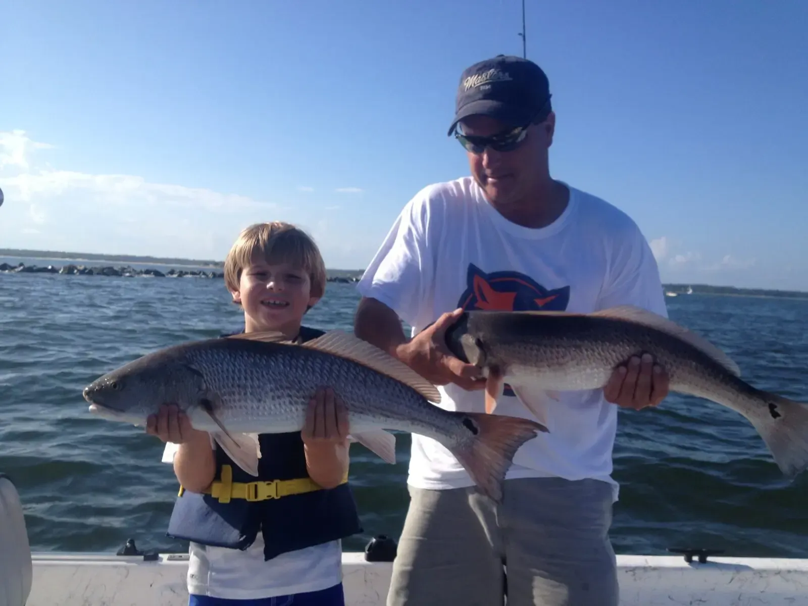 Two people on a boat holding large fish on a sunny day