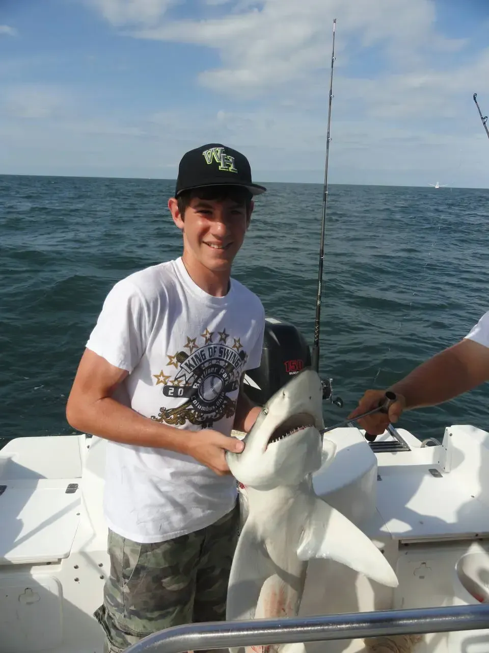 Person on a boat holding a shark with the ocean behind him.