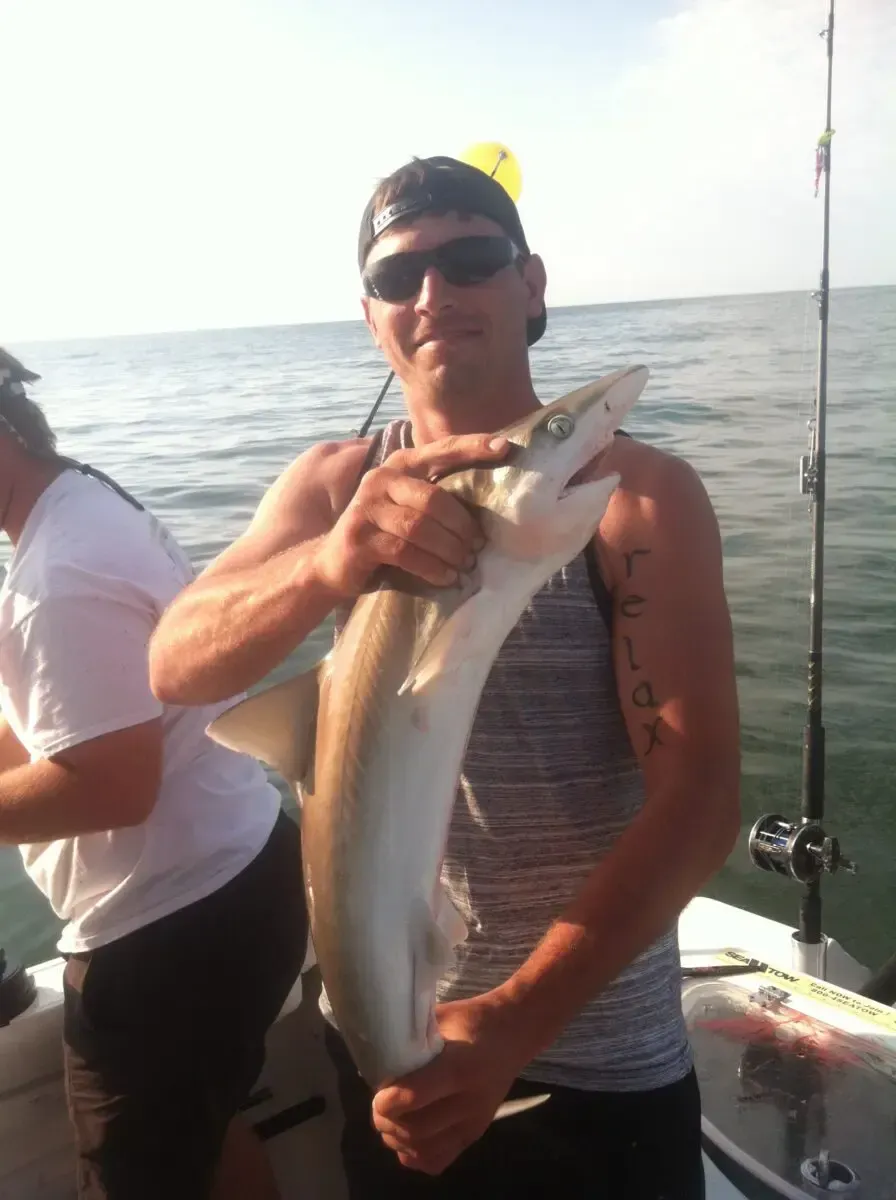 Person on a boat holding a large fish, with the ocean in the background.