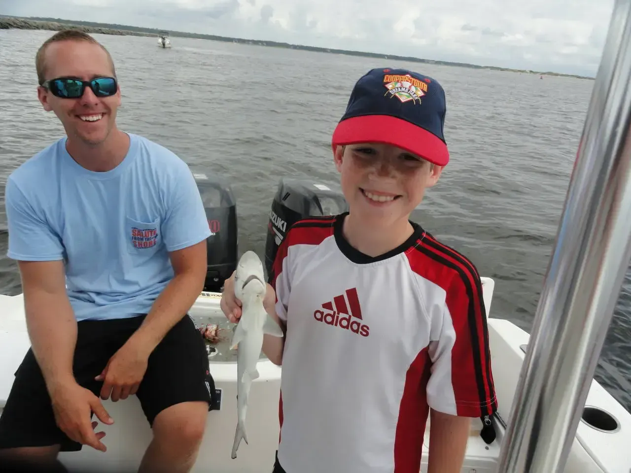 Two people on a boat, smiling and holding up a fish on the water