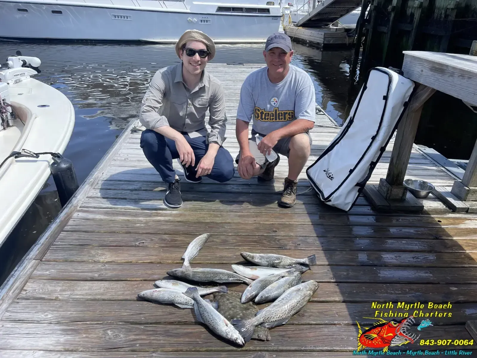 Two people kneel on a dock beside several fish, with boats moored on both sides.