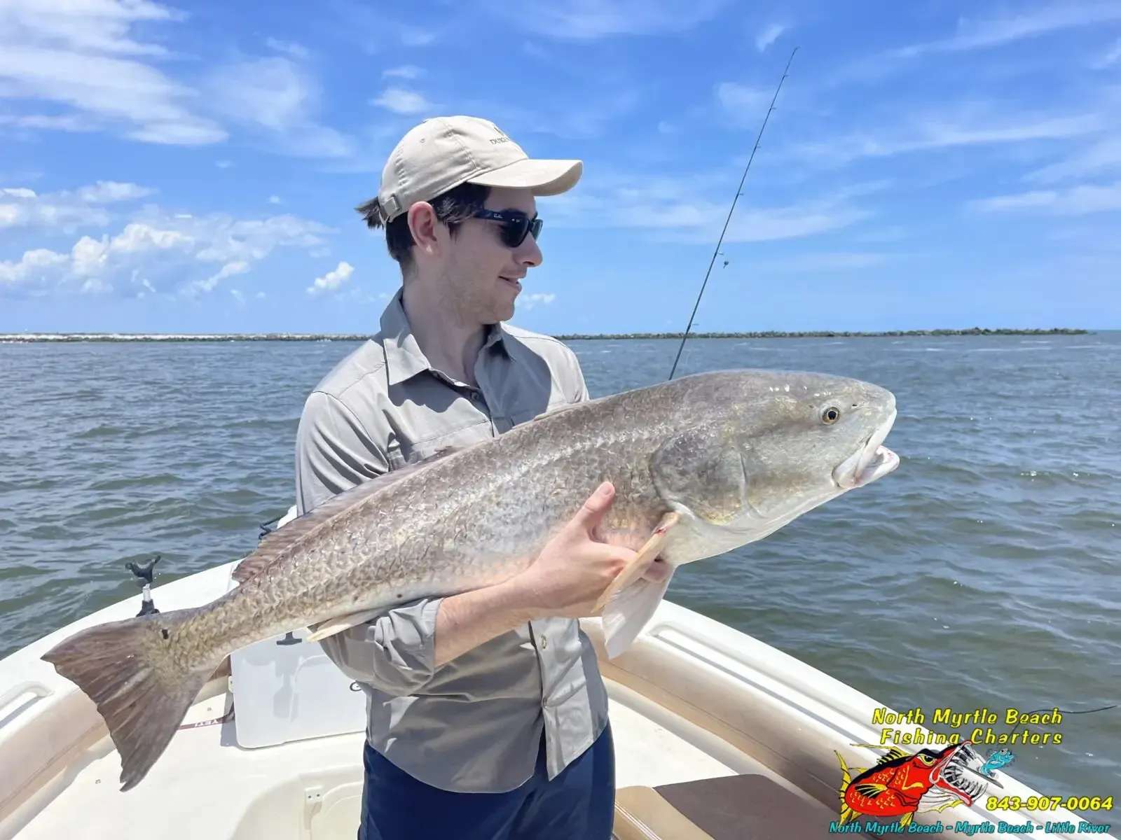 Person holding a large fish on a boat in open water, wearing a hat and sunglasses.