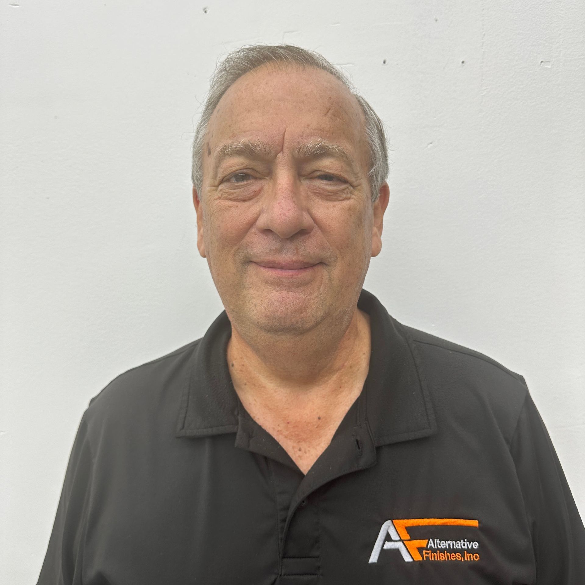 Man in black polo shirt smiles in front of white wall; Alternative Futures logo on shirt.