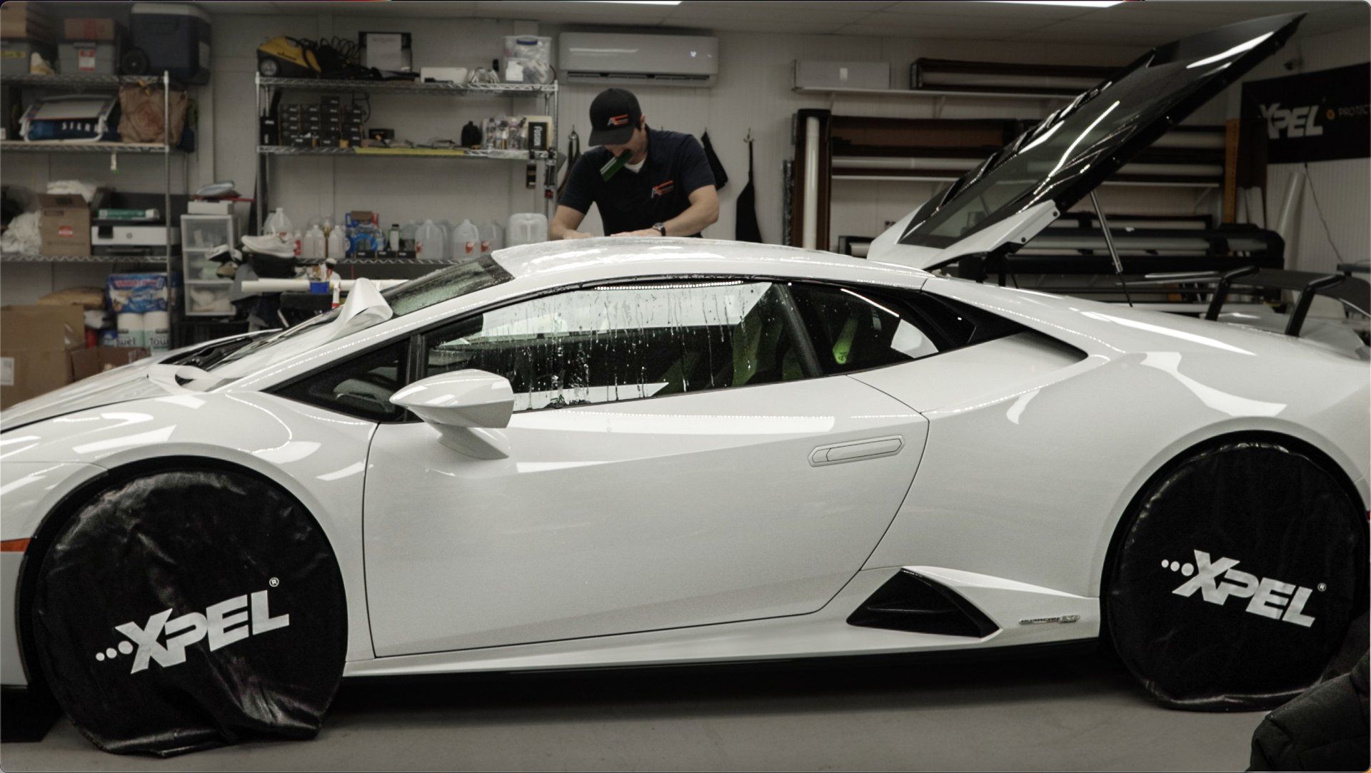 Man working on white Lamborghini with open door in a shop. Wheel covers display 