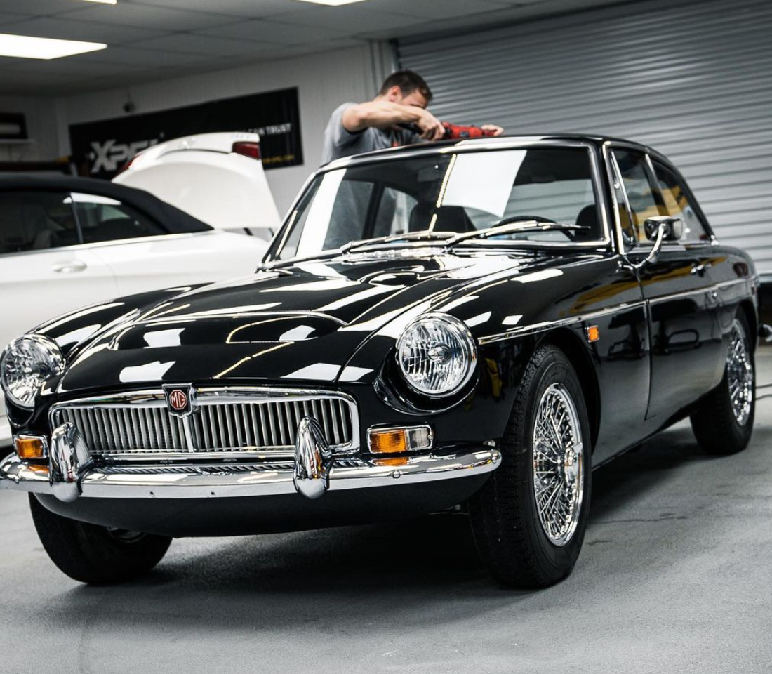 Black classic car with chrome detailing, being paint corrected in preparation for applying Xpel products