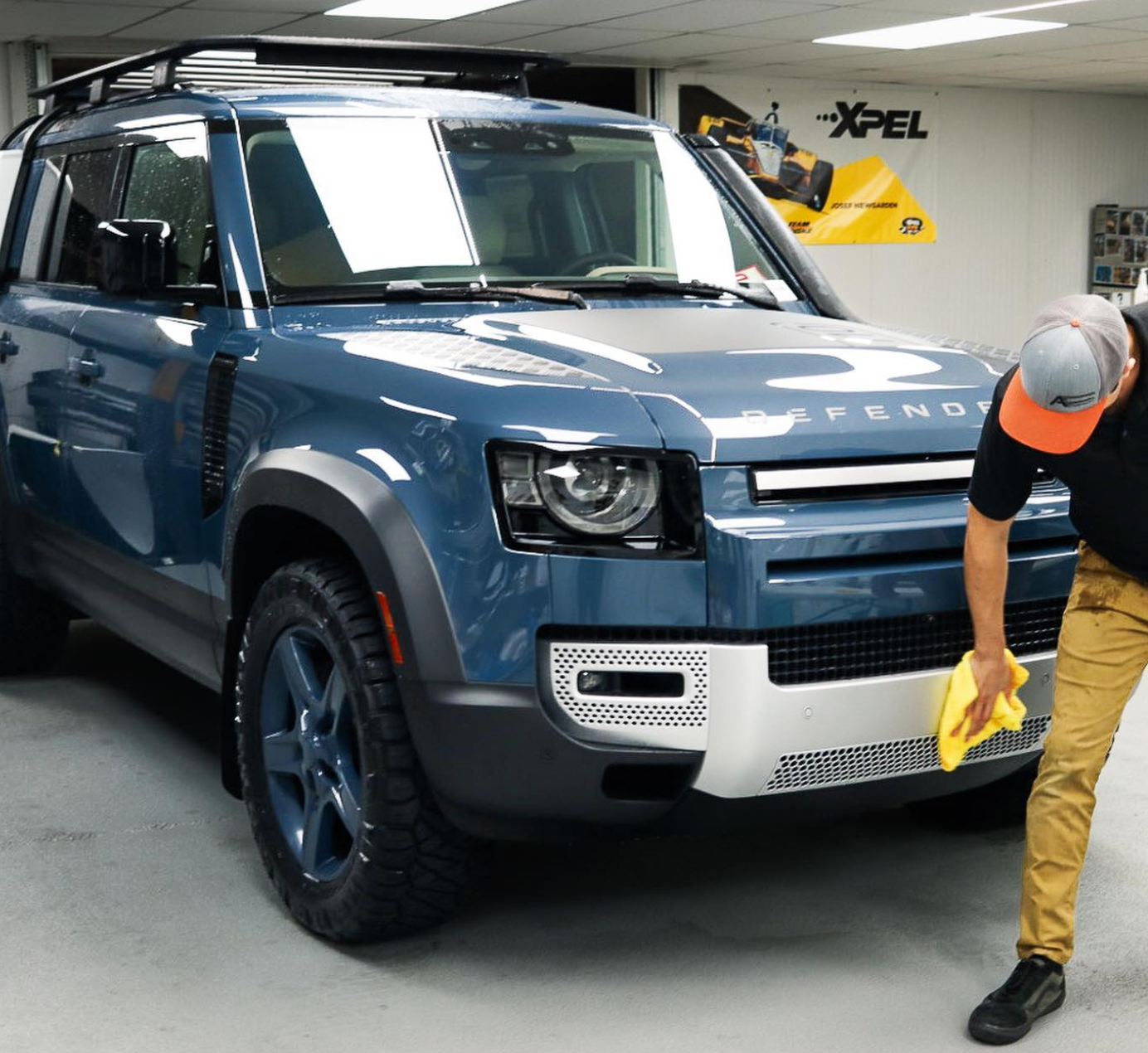 Man wiping down a blue Land Rover Defender truck after installing Xpel paint protection film.