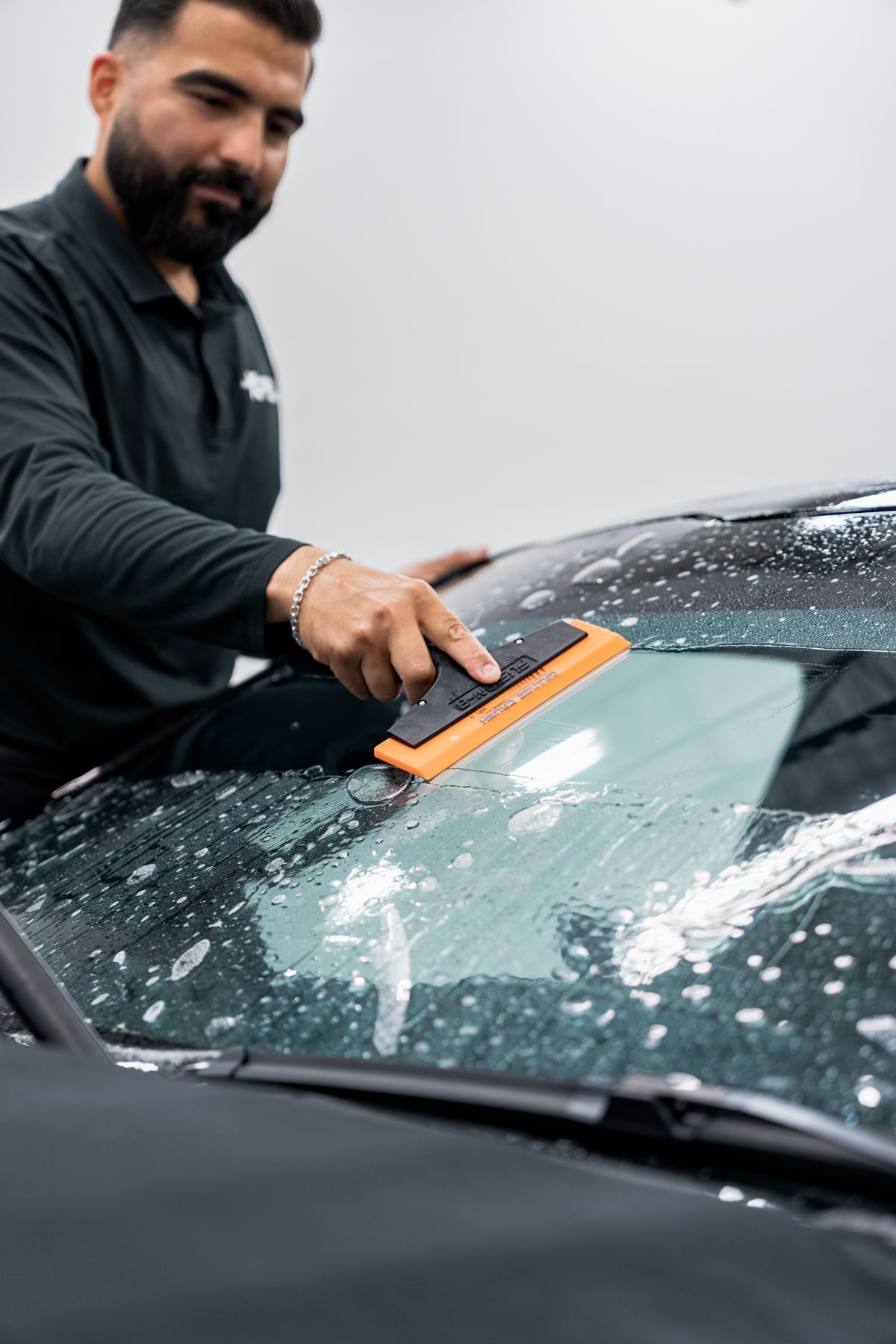 Man using a squeegee on a car windshield, applying windshield protection film.