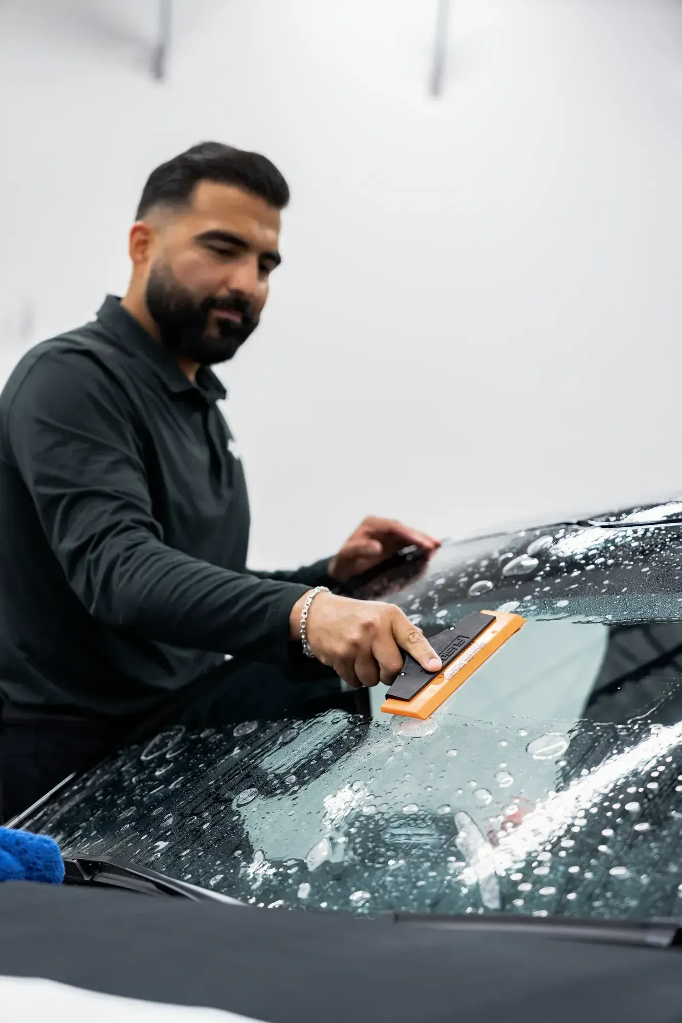 Man using a squeegee on a car windshield, applying windshield protection film.
