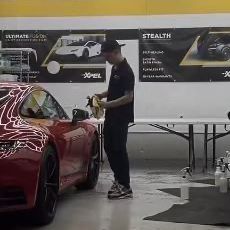 Man in black outfit cleaning red sports car in a shop.