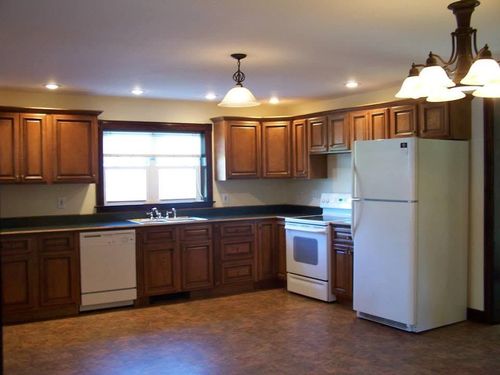 Wooden kitchen with white appliances, dark countertops, and a window over the sink