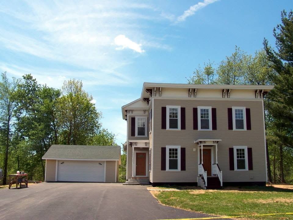 Two-story beige house with burgundy shutters and detached garage on a sunny suburban lot