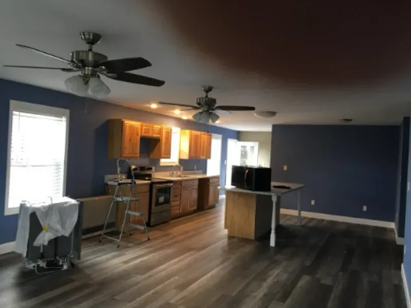 Empty modern kitchen and living area with blue walls, wood floors, and ceiling fans