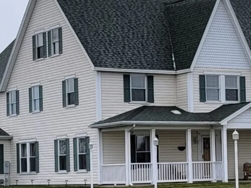 Large white two-story house with gray roof, green shutters, and a covered front porch