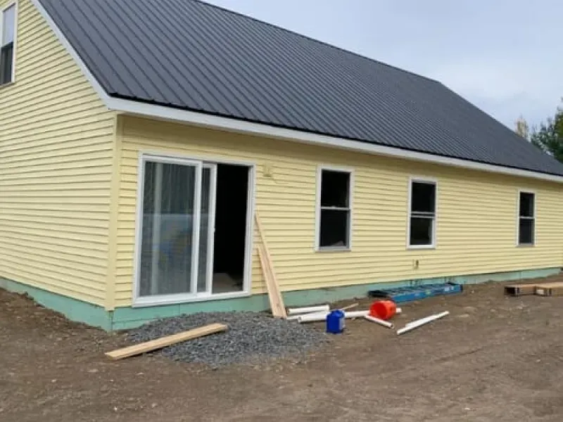 Yellow house with dark gray roof and sliding glass door, construction materials scattered outside