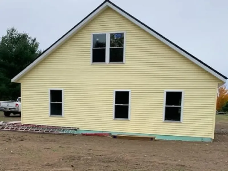 Yellow house exterior with black-trimmed windows and gray roof on bare ground