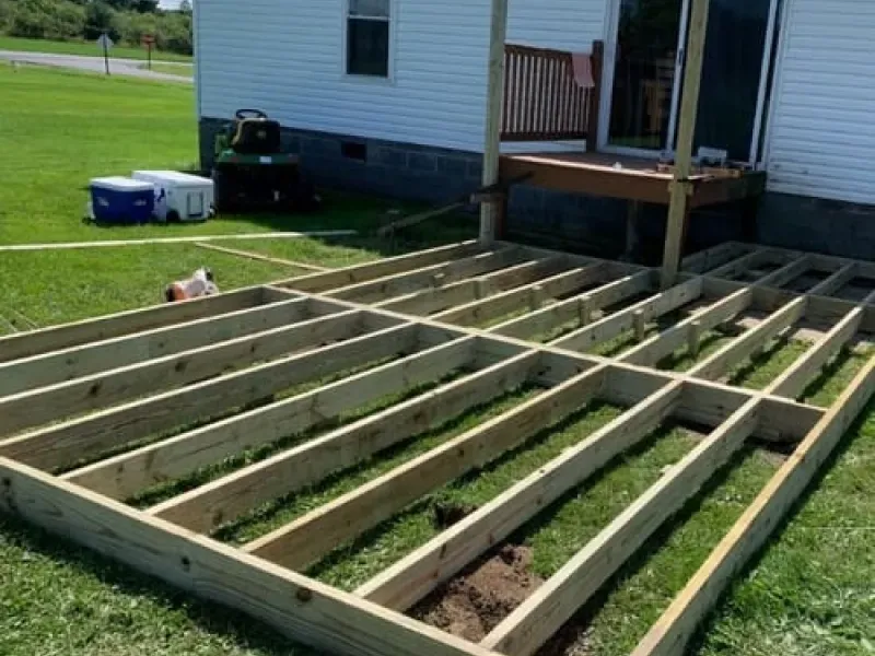 Raised wooden garden beds beside a white house and porch on a sunny lawn