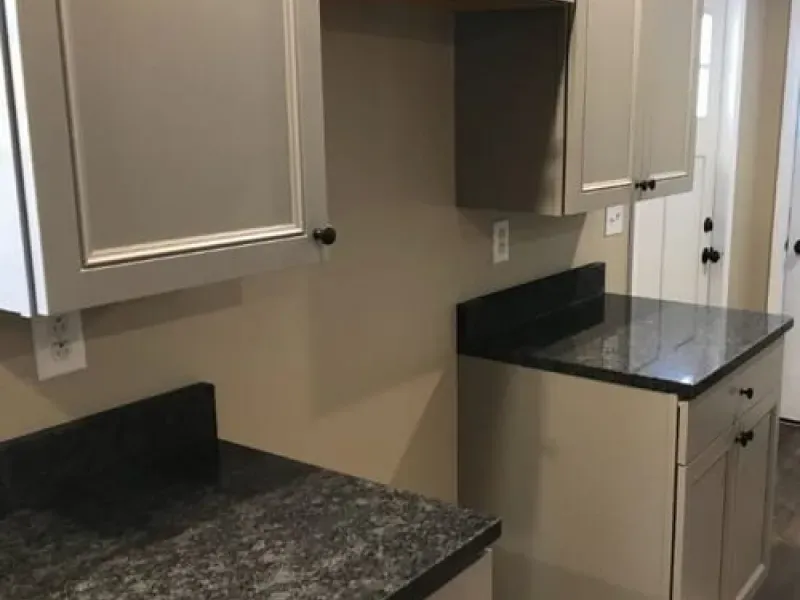 Empty kitchen with gray cabinets, dark countertops, and a beige wall.