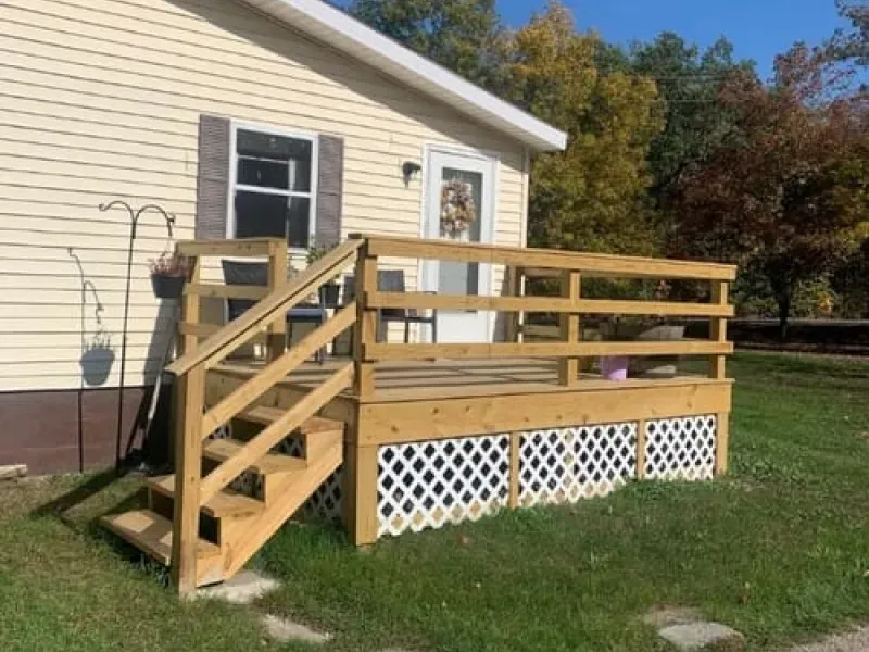 Wooden wheelchair ramp with railings attached to a beige house, over white lattice skirting.