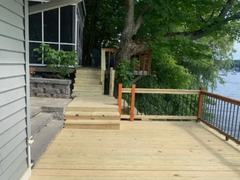 Wooden deck with steps leading to a house by a wooded lakeside, with railing and water view.