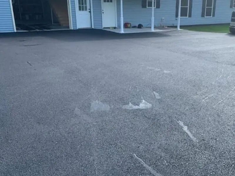 Cracked asphalt driveway in front of a light blue house with a covered porch
