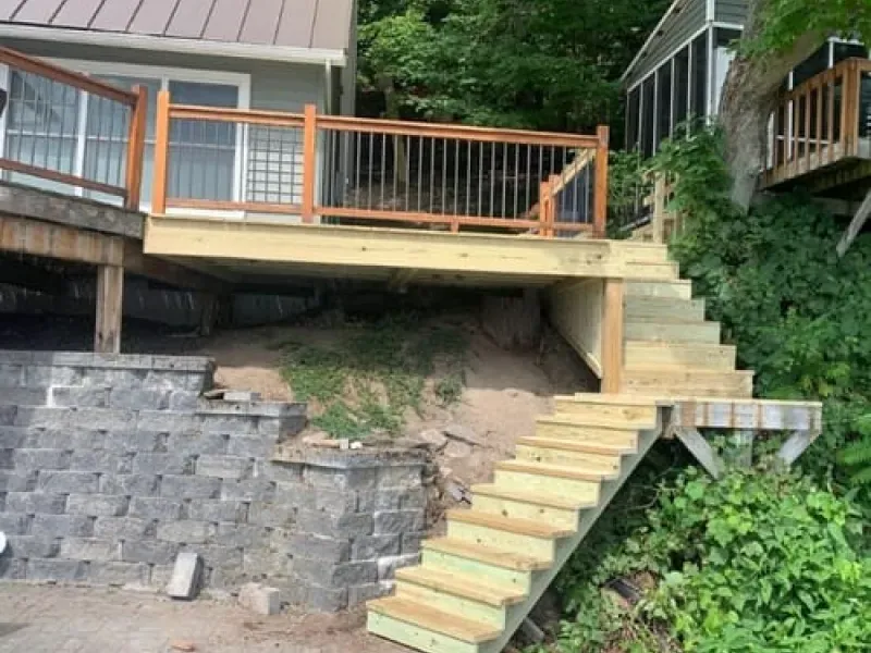 Wooden deck with stairs and railing on a hillside beside a house