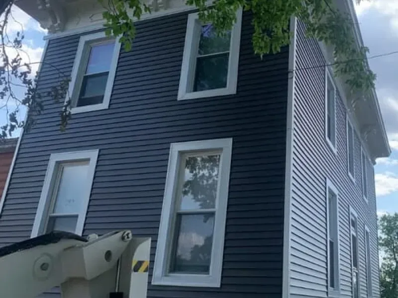 Dark blue house exterior with white-trimmed windows and a tree overhead