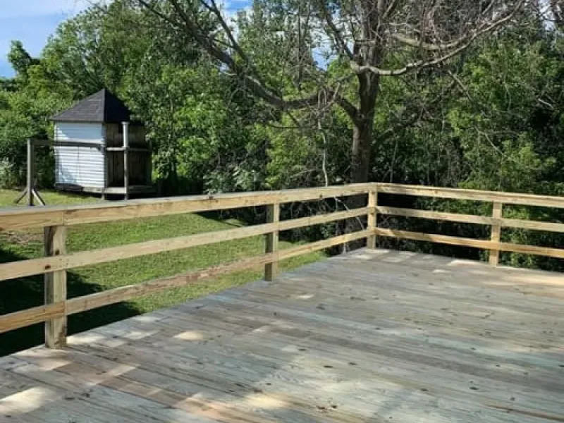 Wooden deck with railing overlooking a grassy yard and small shed among trees