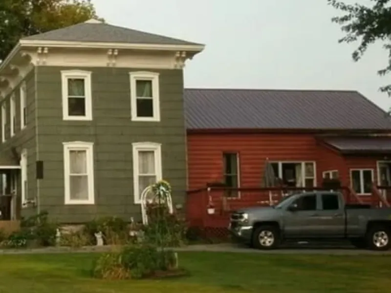 Gray two-story house beside red house with a pickup truck parked in front
