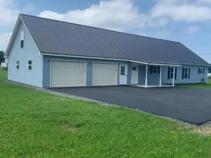Gray building with two garage doors and a covered porch beside a paved driveway