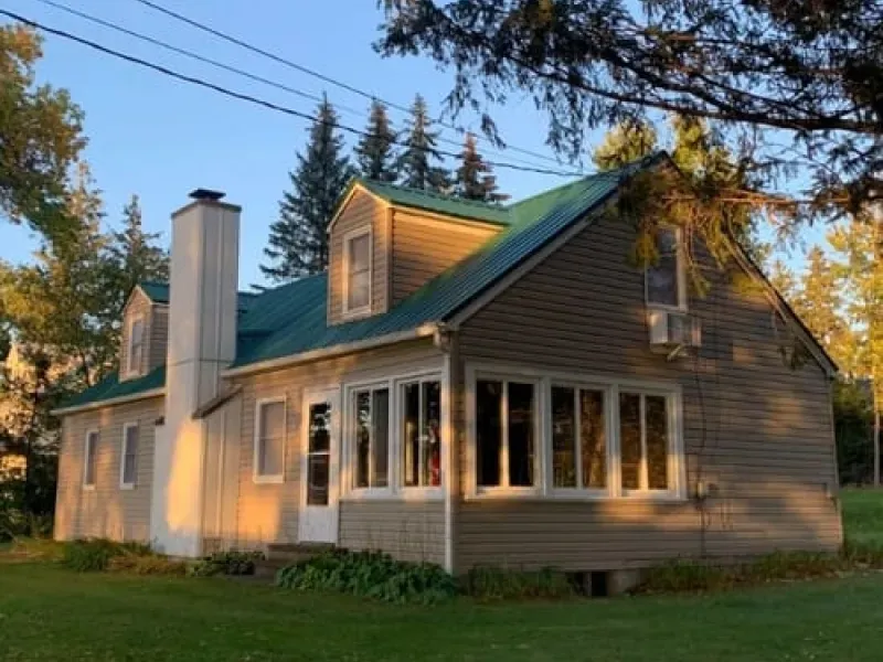 Sunlit gray house with green roof and white chimney among trees at dusk