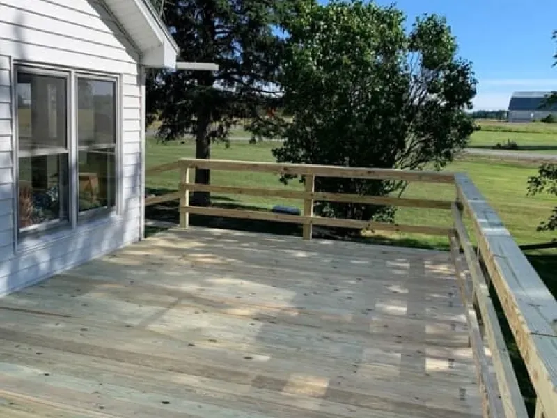 Wooden deck beside a house, overlooking a grassy yard and trees.