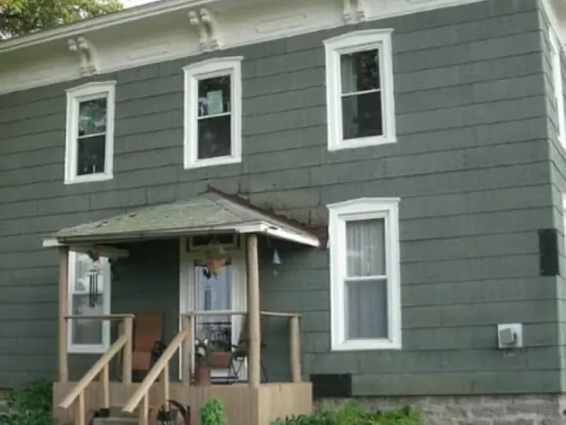 Gray two-story house with a small covered porch and wooden steps in front.