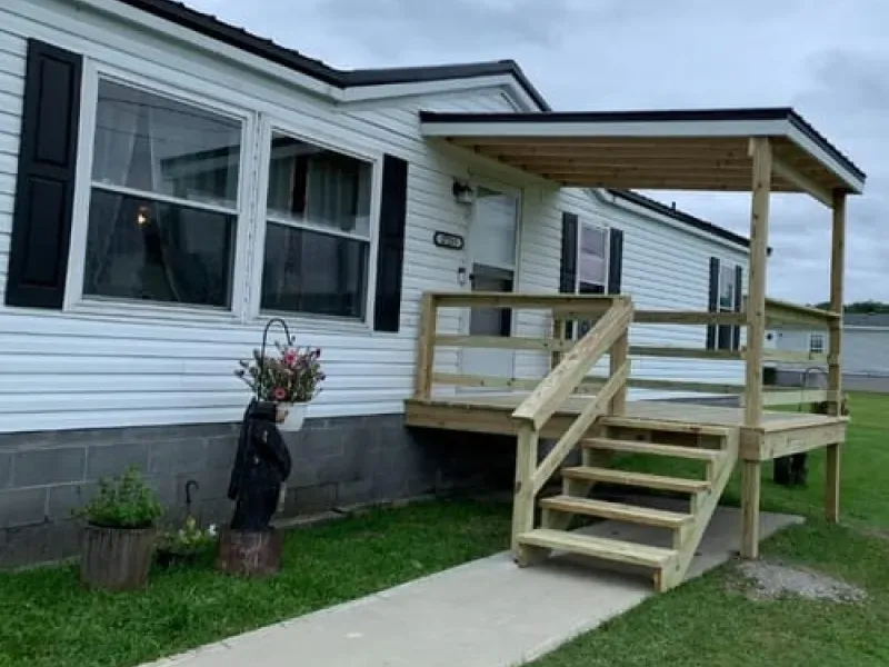 White house exterior with a small wooden porch, steps, and a concrete walkway beside a grassy yard