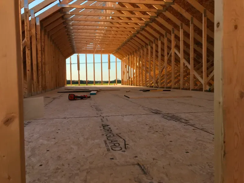 Interior of a wooden-framed house under construction, with exposed beams and plywood flooring.
